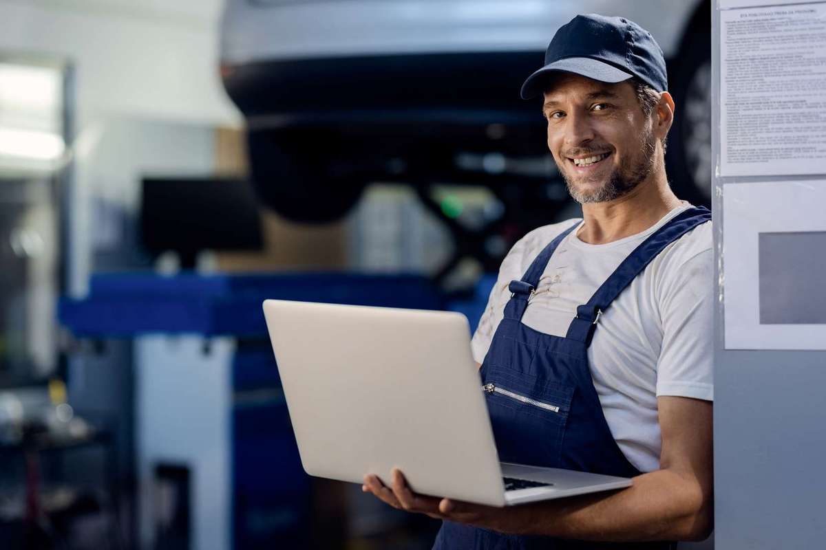 Happy mechanic working on a computer at auto repair shop.